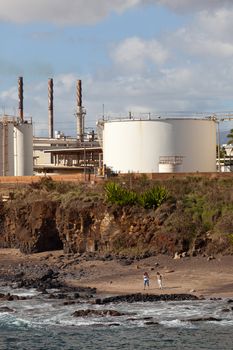 Two women looking on Glass Beach Kauai with refinery behind