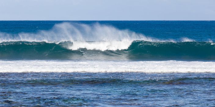 Waves crashing on reef of coast of Kauai and forming rainbow colors in the spray