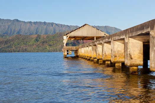Rising sun illuminates the Hanalei pier and Na Pali mountains in Kauai