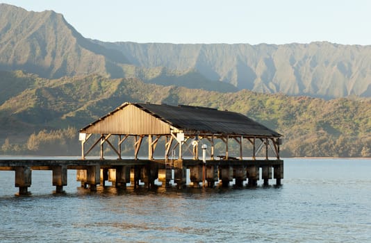 Rising sun illuminates the Hanalei pier and Na Pali mountains in Kauai