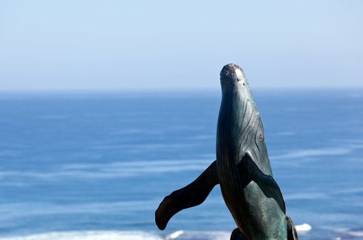 Bronze statue of whale breaching from  sea with ocean in the background