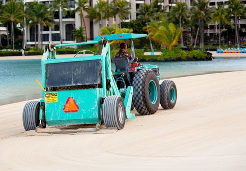 Tractor sweeping sand beach by ocean in front of hotel in Hawaii