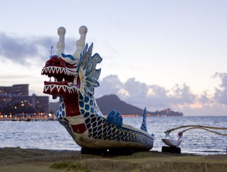 Dragon shaped head on traditional canoe on sand in Waikiki with Diamond Head