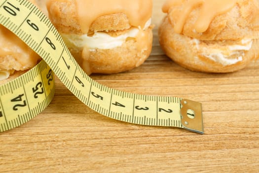 concept of slimming, closeup of caramel cakes with measuring tape on desk