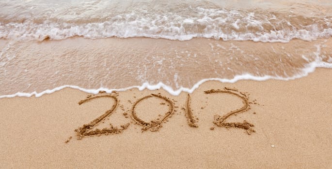 2012 written in sand on beach with sea waves starting to erase the word