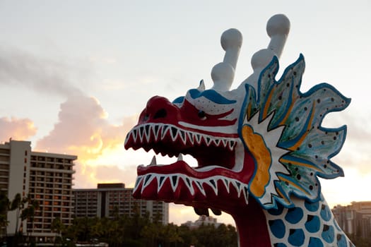Dragon shaped head on traditional canoe on sand in Waikiki with hotels