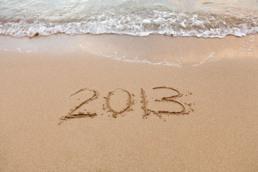 2013 written in sand on beach with sea waves starting to erase the word