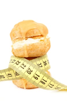 concept of slimming, caramel cakes with measuring tape on white background