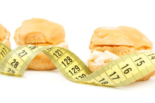 concept of slimming, caramel cakes with measuring tape on white background