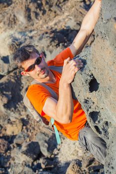 Young man in glasses with backpack climbing indoor wall. Vertical view