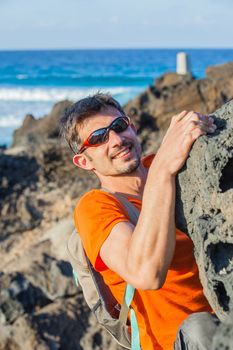 Young man in glasses with backpack climbing indoor wall. Backround sea