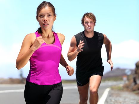 Runners - couple running training for marathon. Sport woman and man jogging on road outside. Athletic female runner and male fitness model running at speed. Young Caucasian man and beautiful Asian woman in nature.