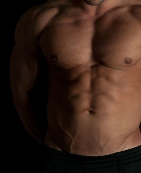 Muscular male torso of bodybuilder on black background
