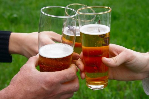 three glass with beer in men hands over green grass field