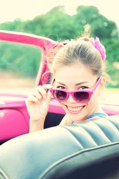 Vintage woman in pink retro car. Retro vintage processed photo of girl on road trip driving in vintage cabriolet car during summer holidays.