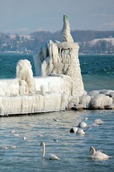 Lighthouse covered with icicles and swan on the lake of Geneva at Nyon, Switzerland