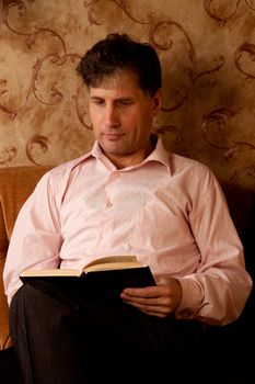 Portrait of middle-aged man reading a book in the black cover at home