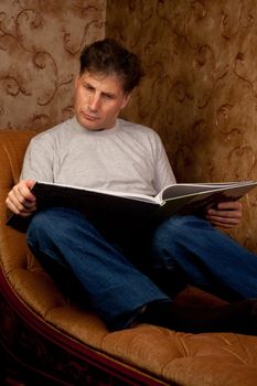 Portrait of middle-aged man reading a book in the black cover at home