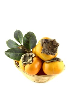 Set of persimmon fruit with leaves in straw basket.