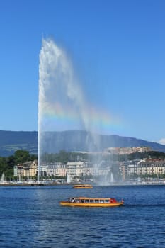 Water fountain with rainbow and famous yellow "mouette" boat on the Geneva lake by beautiful summer day, Geneva, Switzerland