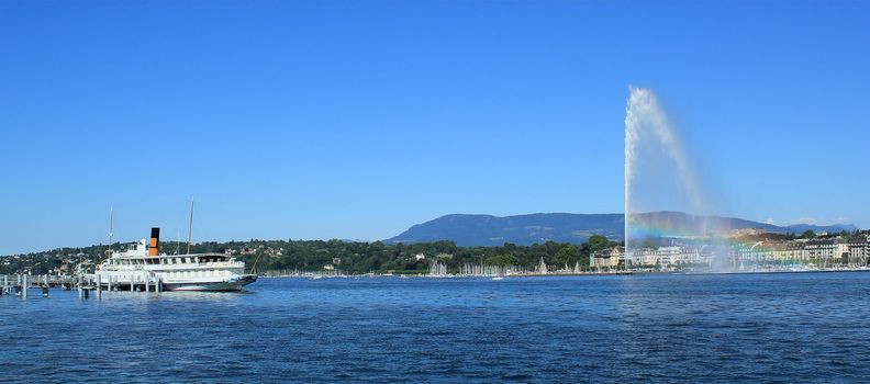 Water fountain with rainbow and old steamboat on the Geneva lake by beautiful summer day, Geneva, Switzerland