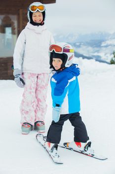 Happy brother and sister in ski goggles and helmets plaing on the downhill in wintertime