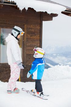 Happy brother and sister in ski goggles and helmets plaing on the downhill in wintertime