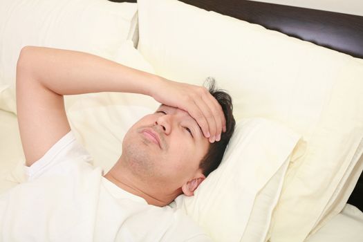 Close up of young man lying down in bed taking temperature and having flu