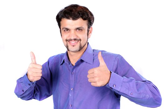 A young Indian man showing the winning sign thumbs up, on white studio background.