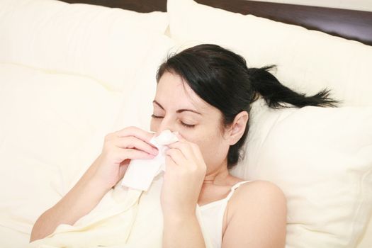 Closeup of gorgeous caucasian woman with cold sneezing into tissue over white background