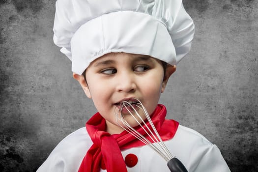 Little boy cook in uniform over vintage background playing with cookware