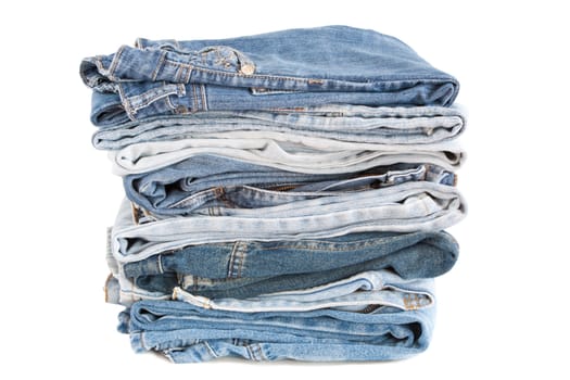 A pile of eight pairs of blue jeans in different shades over a white background.