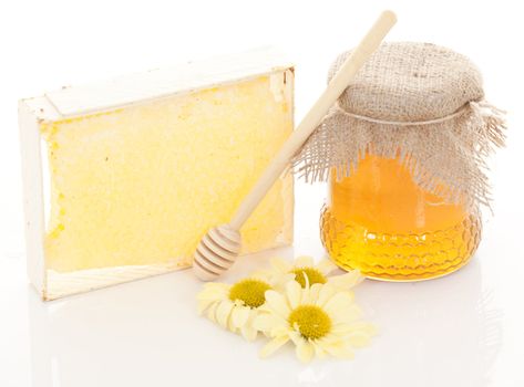 Pot of honey and wooden stick are on a table.