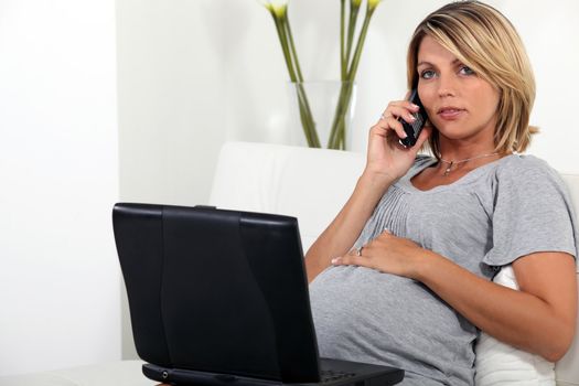 Pregnant woman sitting on the sofa with a laptop and telephone