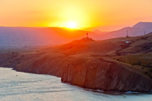 Steep cliff at the edge of the sea at sunset, on the background of the Crimean mountains