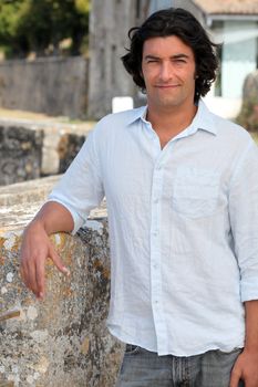 Man with long hair leaning on an old stone wall