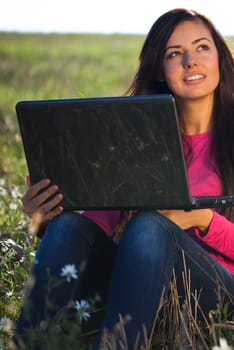 young beautiful woman with a laptop sitting in the field on sky background 