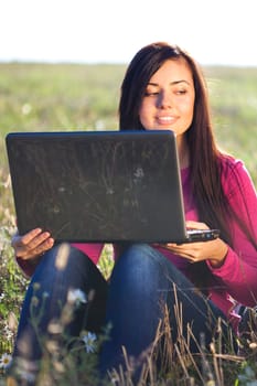 young beautiful woman with a laptop sitting in the field on sky background 