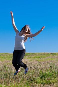 young beautiful woman jumping into the field against the sky