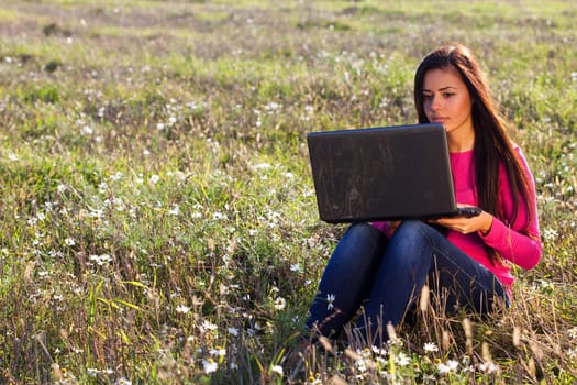 young beautiful woman with a laptop sitting in the field on sky background 