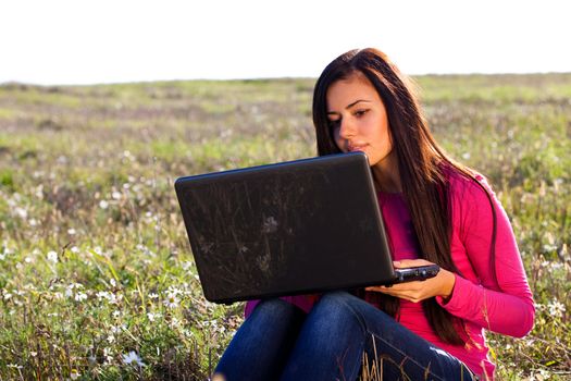 young beautiful woman with a laptop sitting in the field on sky background 