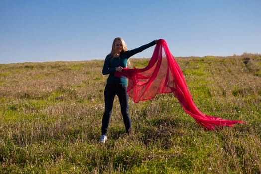 young beautiful woman jumping with tissue into the field against the sky