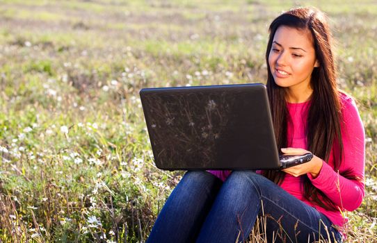 young beautiful woman with a laptop sitting in the field on sky background 