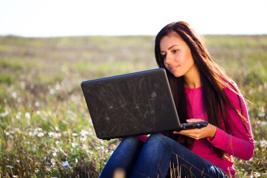 young beautiful woman with a laptop sitting in the field on sky background 