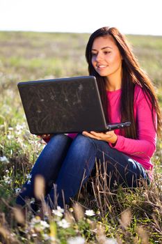 young beautiful woman with a laptop sitting in the field on sky background 