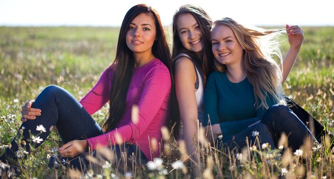 three young beautiful woman sitting in a field on the  sky background 