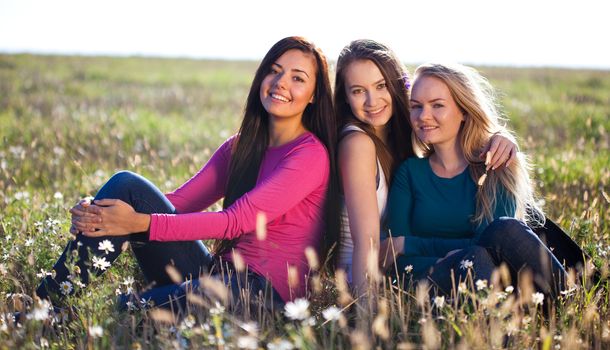 three young beautiful woman sitting in a field on the  sky background 