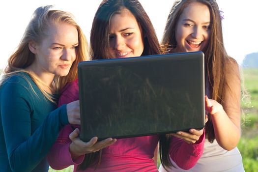 three young beautiful woman with a laptop in the field on sky background 