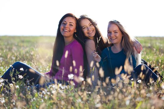 three young beautiful woman sitting in a field on the  sky background 