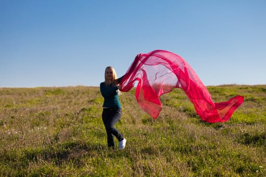 young beautiful woman jumping with tissue into the field against the sky